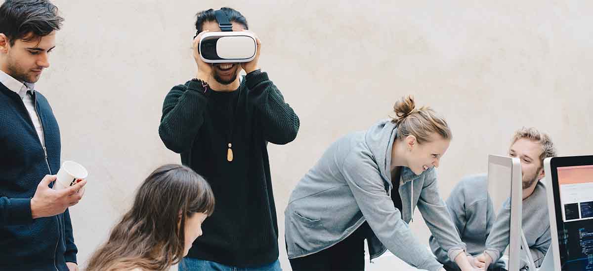 male computer programmer using VR glasses while colleagues working in office