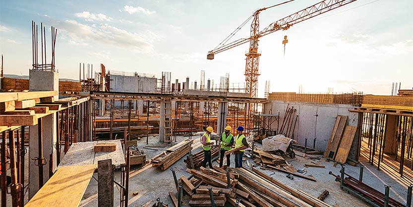 Construction industry concept - architects and engineers discussing work progress between concrete walls, scaffolds and cranes.