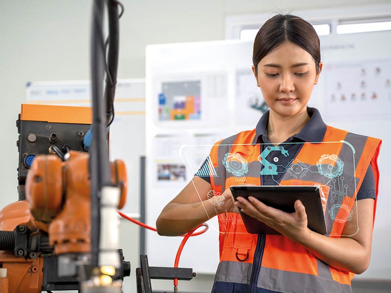 A lady wearing a safety orange vest, at a warehouse, holding a tablet showing automation technologies 
