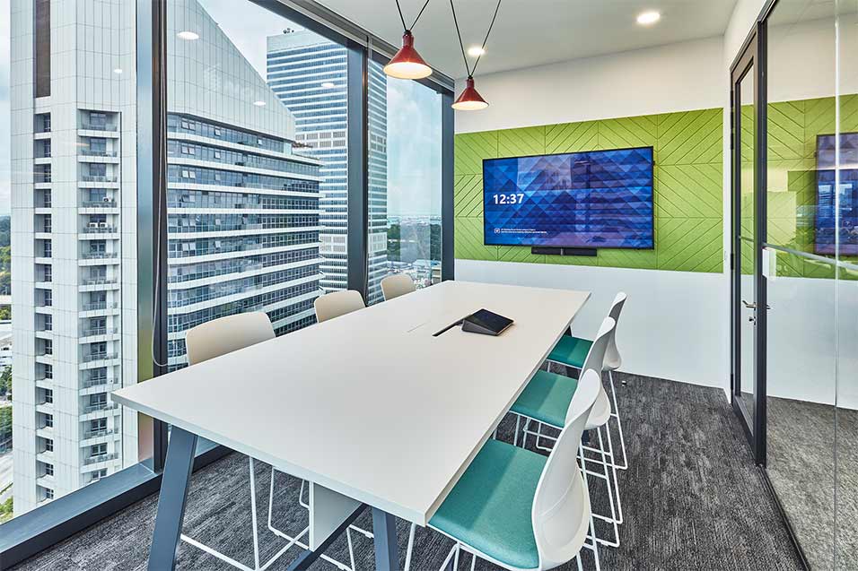 Modern meeting room with video conferencing technology and floor-to-ceiling window with view of business park