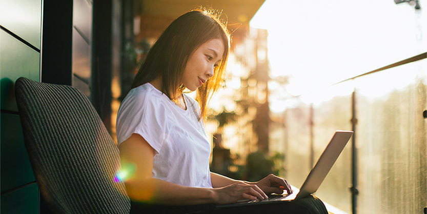 Young Asian woman relaxing on balcony and using laptop