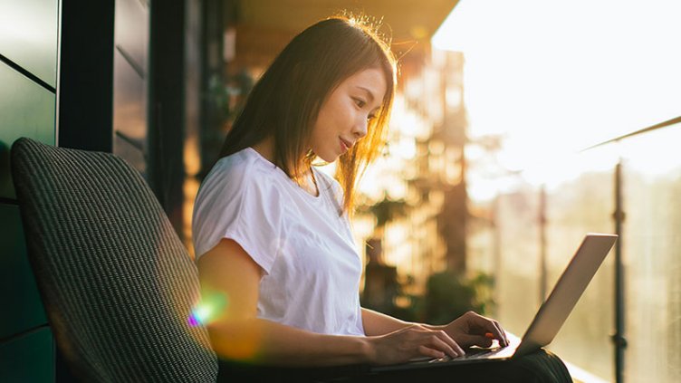 Young Asian woman relaxing on balcony and using laptop