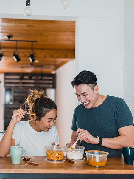 Asian couple laughing and sharing a meal in domestic kitchen