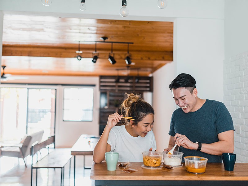 Asian couple laughing and sharing a meal in domestic kitchen