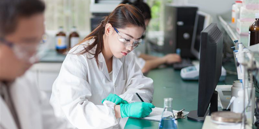 A woman in a lab coat focused on her work while using a computer in a laboratory setting.