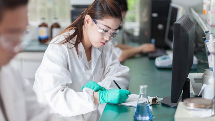 A woman in a lab coat focused on her work while using a computer in a laboratory setting.