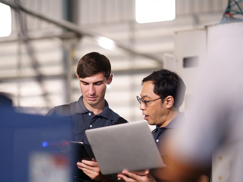 Men looking at computers discussing content while standing in manufacturing space.