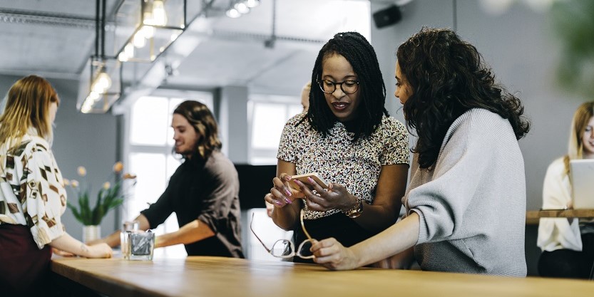 women standing and talking to each at workplace - shows women outrank men